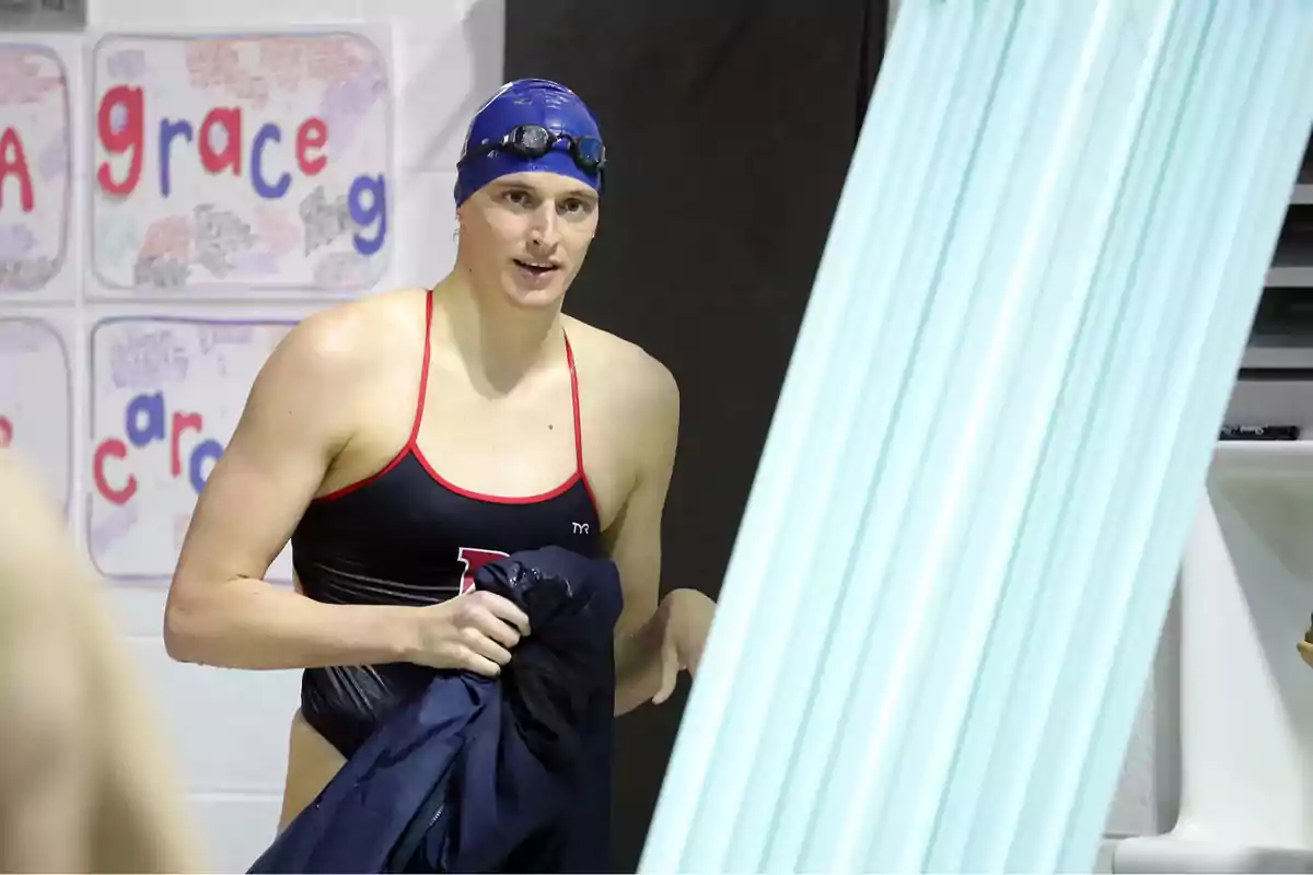 Nadadora con gorro azul y gafas de natación sosteniendo una toalla junto a la piscina