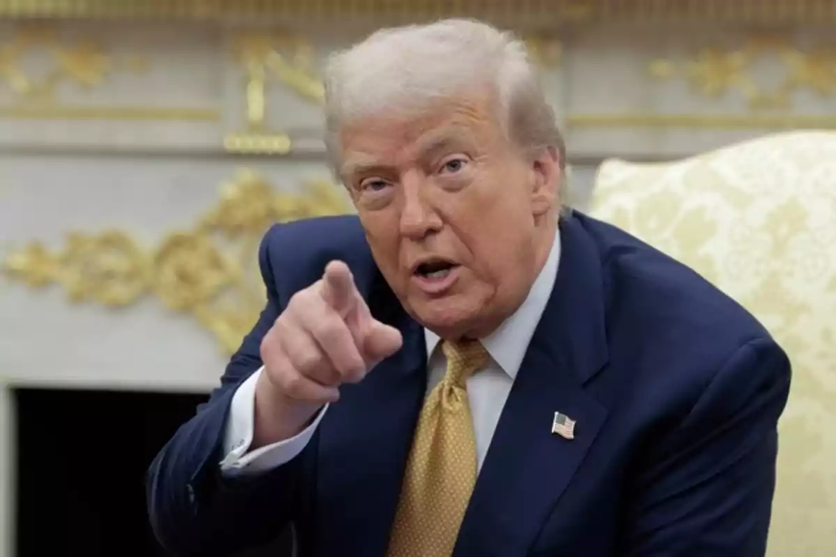 Hombre de cabello rubio con traje azul y corbata amarilla señalando hacia el frente mientras está sentado en una silla elegante Hombre de cabello rubio con traje azul y corbata amarilla señalando hacia el frente mientras está sentado en una silla elegante