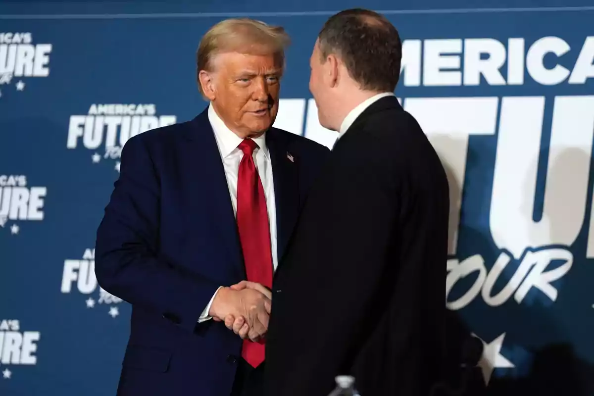 Dos hombres de traje se dan la mano frente a un fondo azul con letras blancas que dicen America's Future Tour