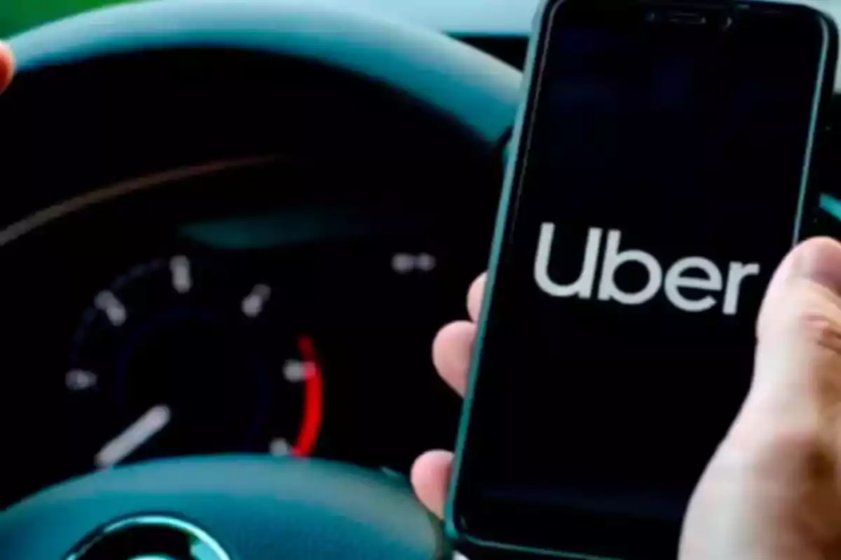 Persona sosteniendo un teléfono móvil con la aplicación de Uber abierta mientras conduce un automóvil Persona sosteniendo un teléfono móvil con la aplicación de Uber abierta mientras conduce un automóvil