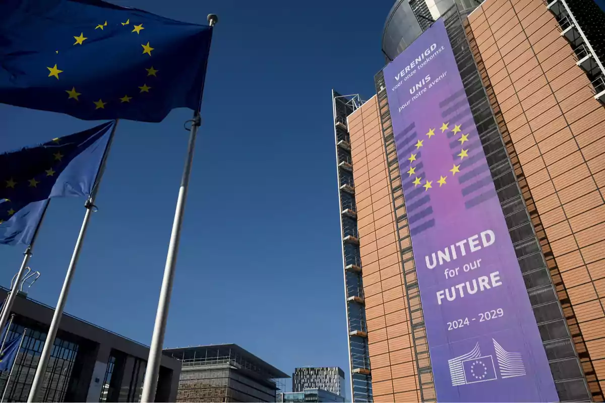 Banderas de la Unión Europea ondeando frente a un edificio con un gran cartel que dice United for our future 2024-2029 bajo un cielo despejado. Banderas de la Unión Europea ondeando frente a un edificio con un gran cartel que dice United for our future 2024-2029 bajo un cielo despejado.