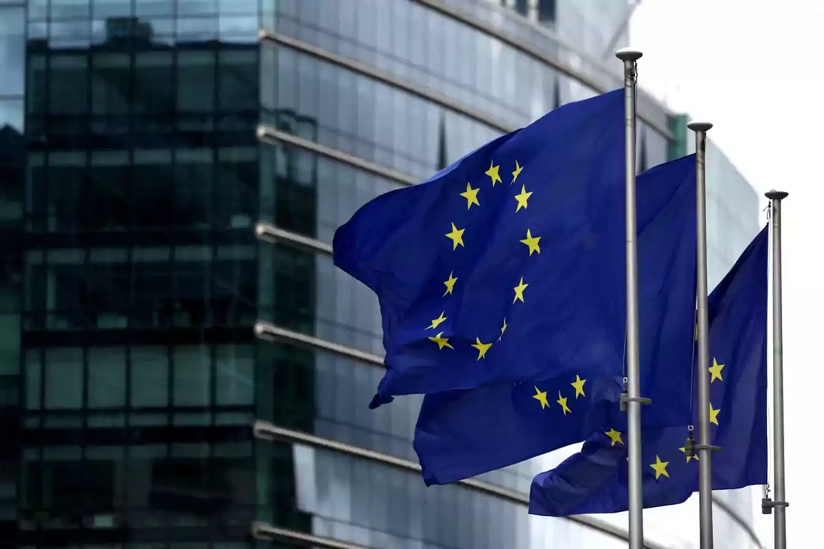 Banderas de la Unión Europea ondeando frente a un edificio moderno de vidrio