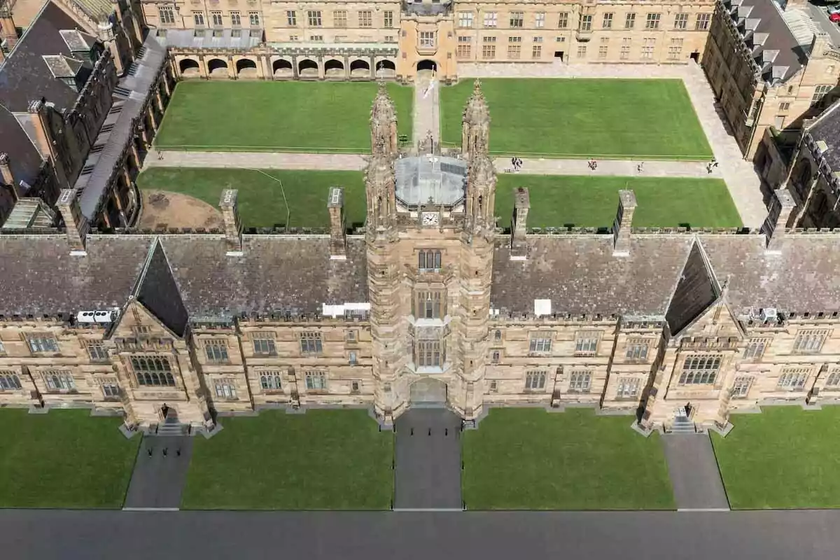 Aerial view of a historic stone building with a large central lawn courtyard surrounded by paths and people walking Aerial view of a historic stone building with a large central lawn courtyard surrounded by paths and people walking