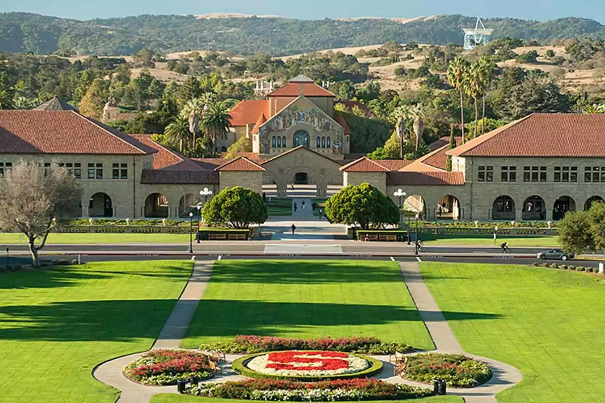 Panoramic view of the Stanford University campus with green gardens, red-roofed buildings, and hills in the background Panoramic view of the Stanford University campus with green gardens, red-roofed buildings, and hills in the background