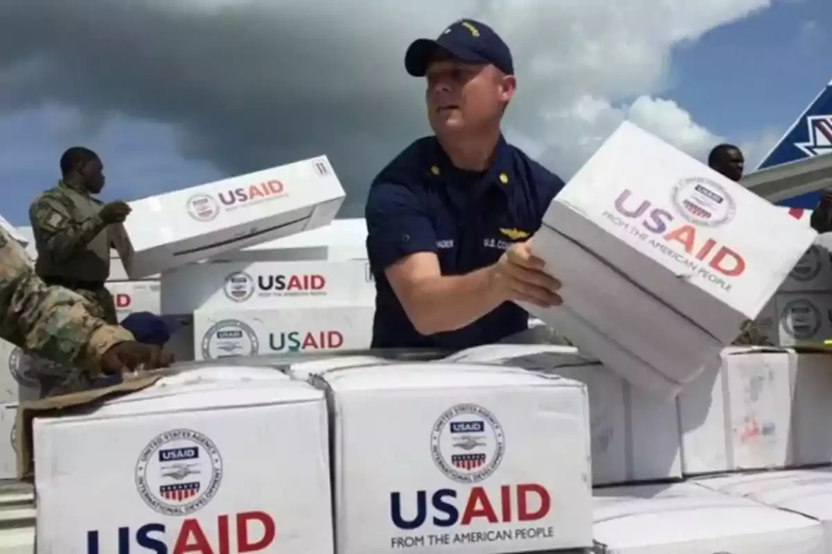 Un grupo de personas con uniforme descarga cajas de ayuda humanitaria de USAID bajo un cielo nublado.