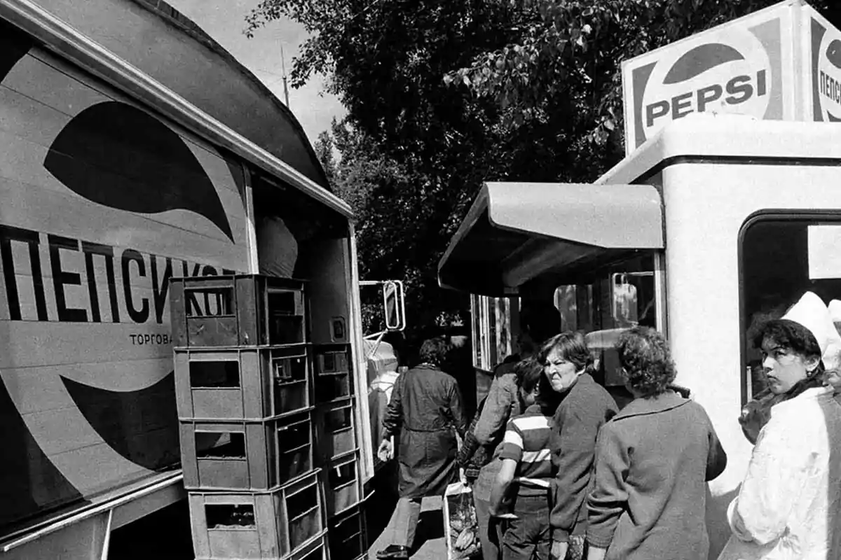 People line up next to a truck and a Pepsi stand in a black-and-white urban scene. People line up next to a truck and a Pepsi stand in a black-and-white urban scene.