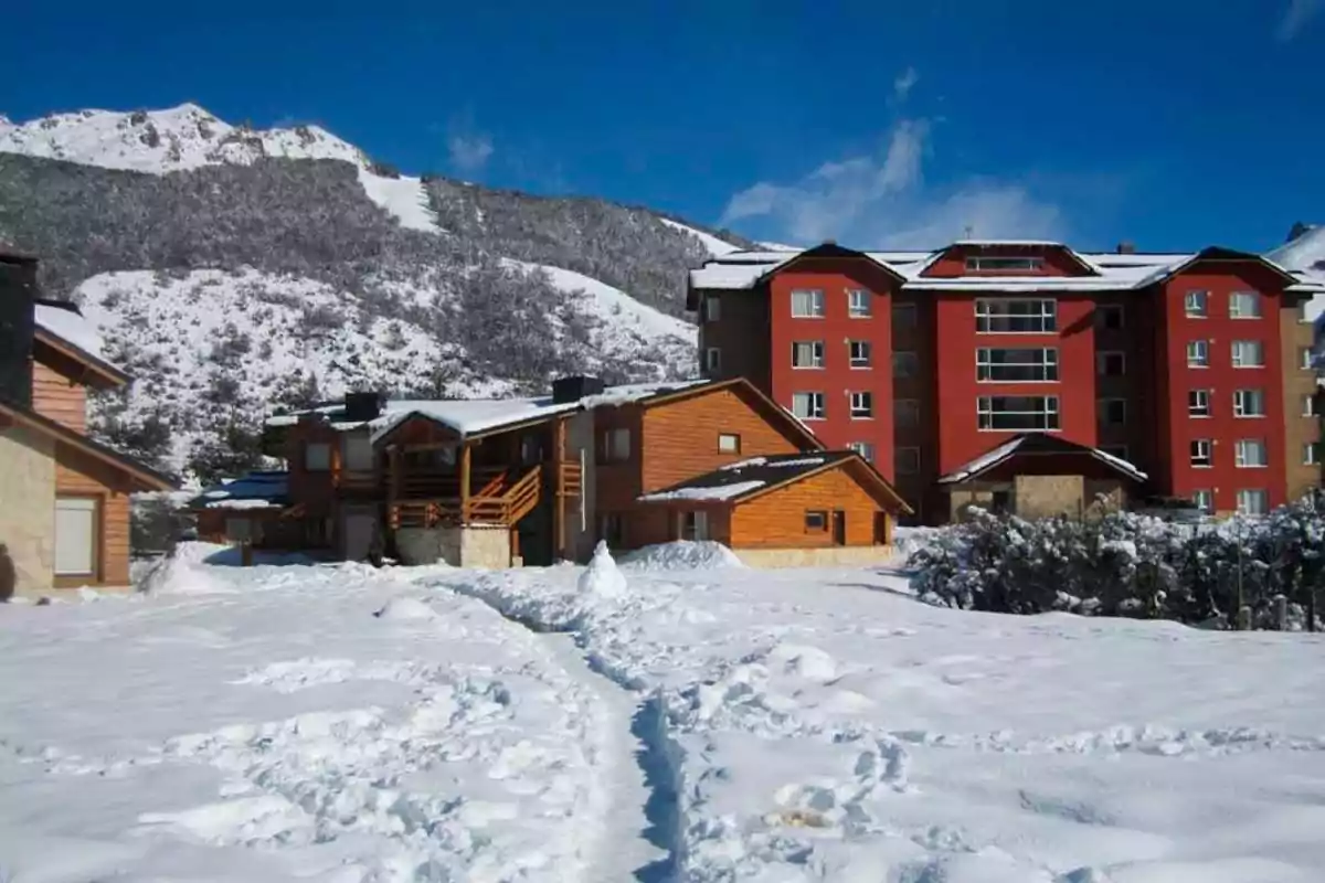 Cabins and buildings surrounded by snow with mountains in the background under a blue sky Cabins and buildings surrounded by snow with mountains in the background under a blue sky