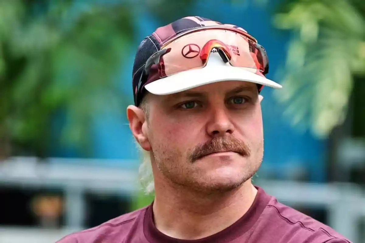 Man with a mustache wearing a cap, sport sunglasses, and a maroon t-jersey in an outdoor setting with vegetation in the background Man with a mustache wearing a cap, sport sunglasses, and a maroon t-jersey in an outdoor setting with vegetation in the background