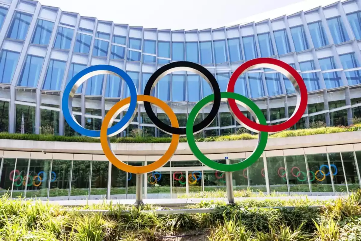 Sculpture of the Olympic rings in front of a modern building with glass windows and vegetation in the foreground