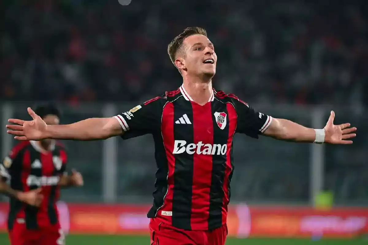 Futbolista con uniforme negro y rojo celebrando un gol con los brazos extendidos en un estadio Futbolista con uniforme negro y rojo celebrando un gol con los brazos extendidos en un estadio