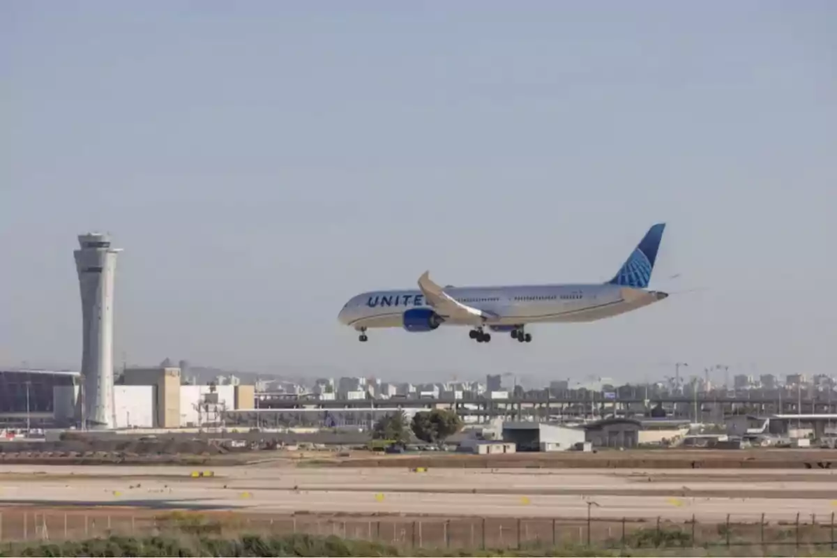 United Airlines passenger plane landing at an airport with the control tower in the background and buildings on the horizon
