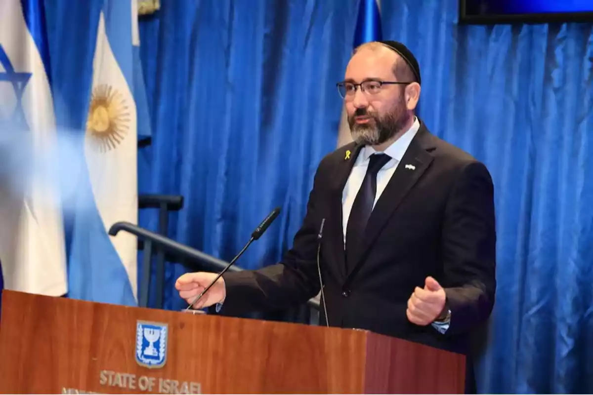 Hombre con barba y gafas hablando en un podio oficial con las banderas de Israel y Argentina de fondo Hombre con barba y gafas hablando en un podio oficial con las banderas de Israel y Argentina de fondo