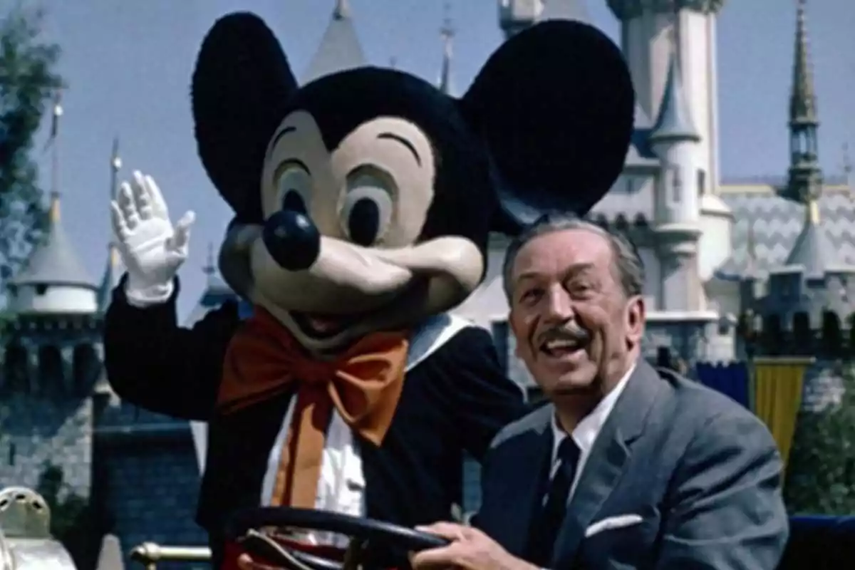 A smiling man next to someone dressed as Mickey Mouse in a theme park with a castle in the background A smiling man next to someone dressed as Mickey Mouse in a theme park with a castle in the background
