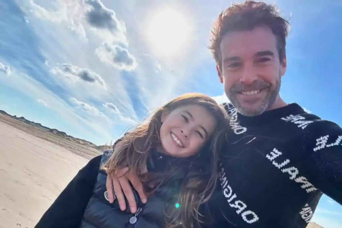 Un hombre y una niña sonríen mientras se toman una selfie en la playa con el sol brillando en el cielo azul y algunas nubes de fondo Un hombre y una niña sonríen mientras se toman una selfie en la playa con el sol brillando en el cielo azul y algunas nubes de fondo
