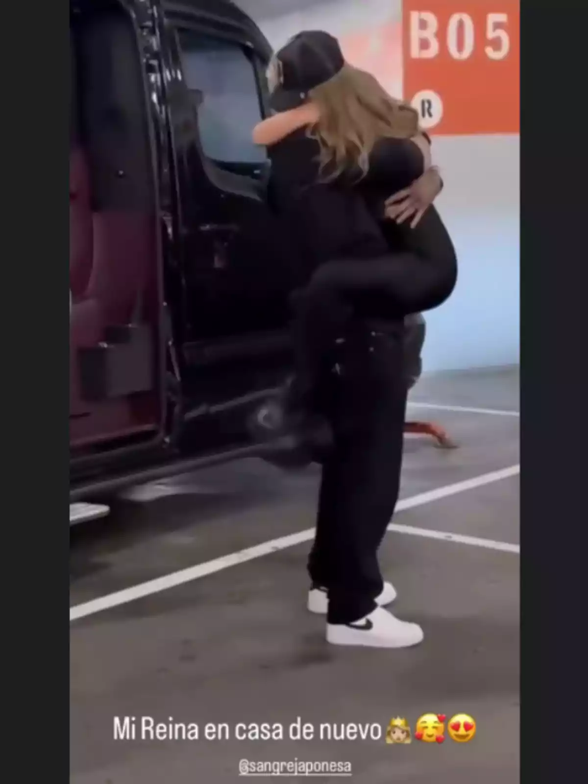 Una persona abraza y carga a otra con alegría junto a una camioneta negra en un estacionamiento, mostrando un reencuentro emotivo. Una persona abraza y carga a otra con alegría junto a una camioneta negra en un estacionamiento, mostrando un reencuentro emotivo.