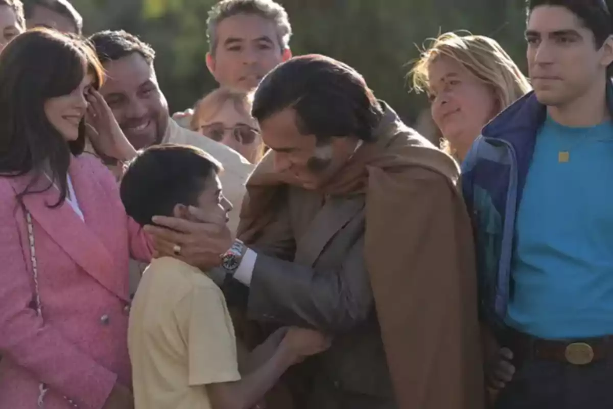 A smiling man affectionately hugs a child while several people watch the scene with joy. A smiling man affectionately hugs a child while several people watch the scene with joy.