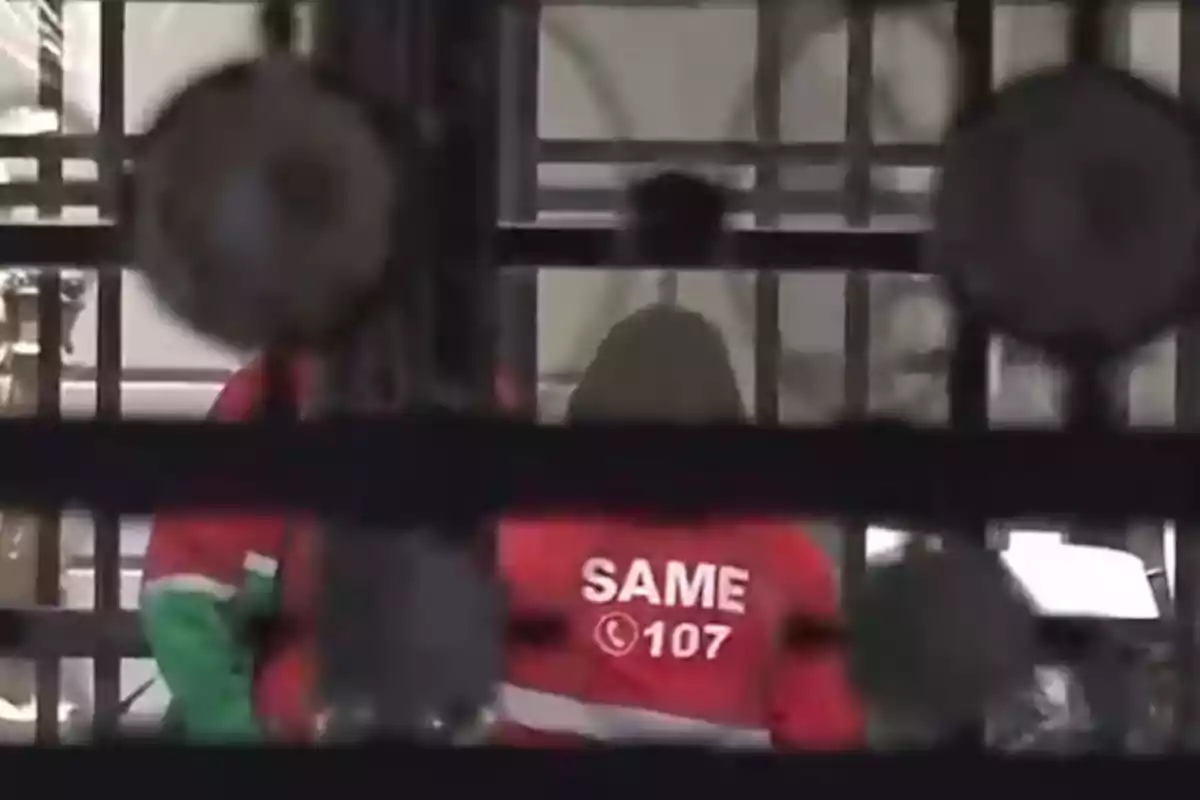 Persona con campera roja de emergencias médicas SAME 107 vista a través de una reja