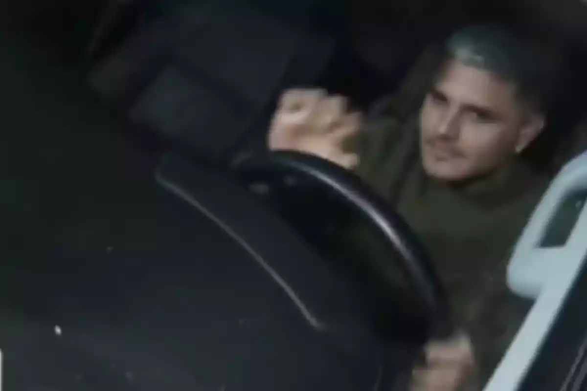 Hombre con cabello corto y teñido de color claro sentado al volante de un automóvil mirando hacia la cámara