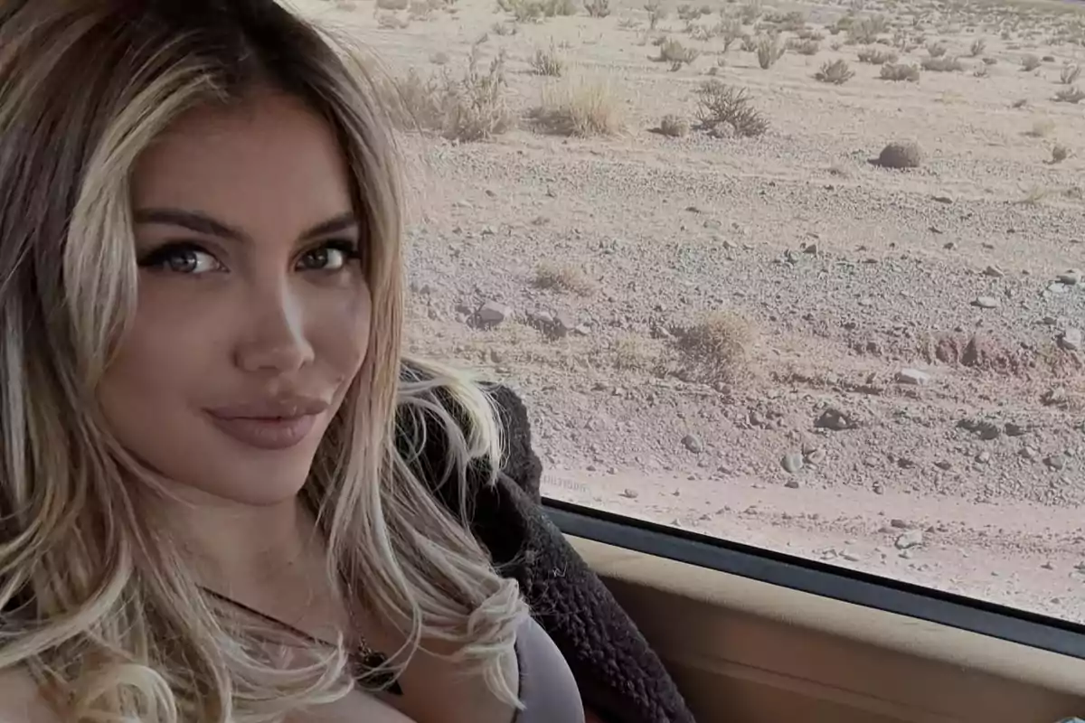 Mujer de cabello rubio sentada dentro de un auto con paisaje desértico al fondo
