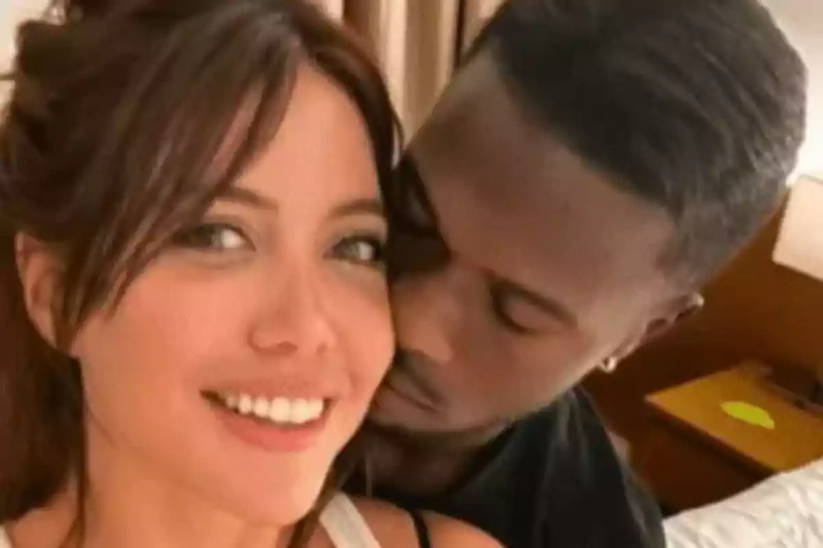 Una pareja abrazada en una habitación sonríe mientras se toma una selfie