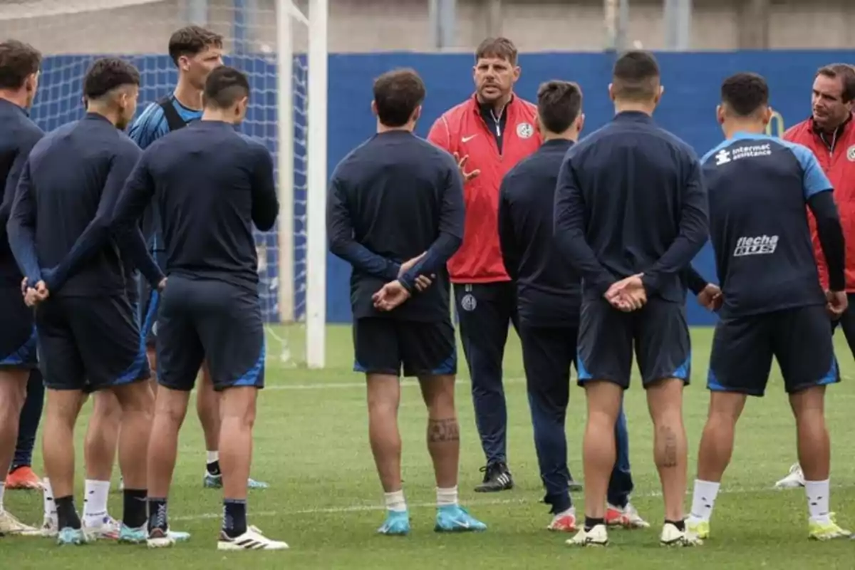 Un grupo de jugadores de fútbol escucha atentamente a su entrenador durante una charla en el campo de entrenamiento Un grupo de jugadores de fútbol escucha atentamente a su entrenador durante una charla en el campo de entrenamiento