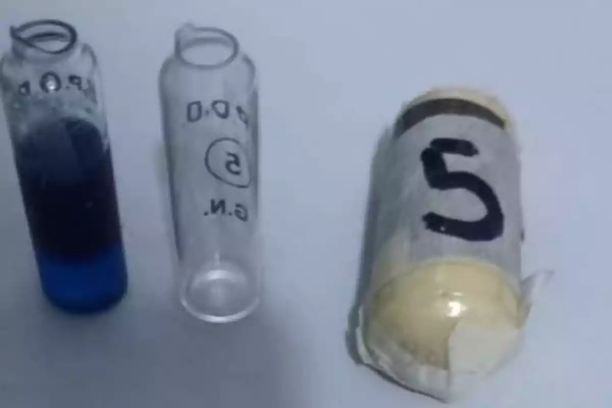 Dos frascos de vidrio pequeños, uno con líquido azul y otro vacío, junto a un cilindro envuelto en cinta con el número 5 escrito