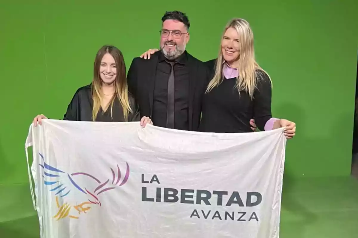 Tres personas sonríen frente a un fondo verde mientras sostienen una bandera blanca con el logo de un águila y el texto La Libertad Avanza Tres personas sonríen frente a un fondo verde mientras sostienen una bandera blanca con el logo de un águila y el texto La Libertad Avanza
