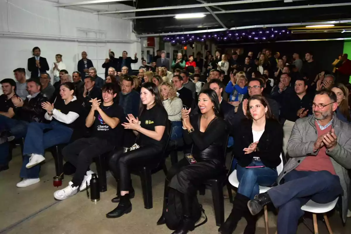 Un grupo numeroso de personas sentadas y aplaudiendo en un evento en un espacio cerrado Un grupo numeroso de personas sentadas y aplaudiendo en un evento en un espacio cerrado