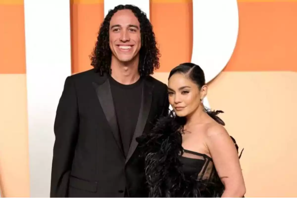 Pareja posando en una alfombra roja con fondo naranja y blanco ambos vestidos de negro elegantes Pareja posando en una alfombra roja con fondo naranja y blanco ambos vestidos de negro elegantes