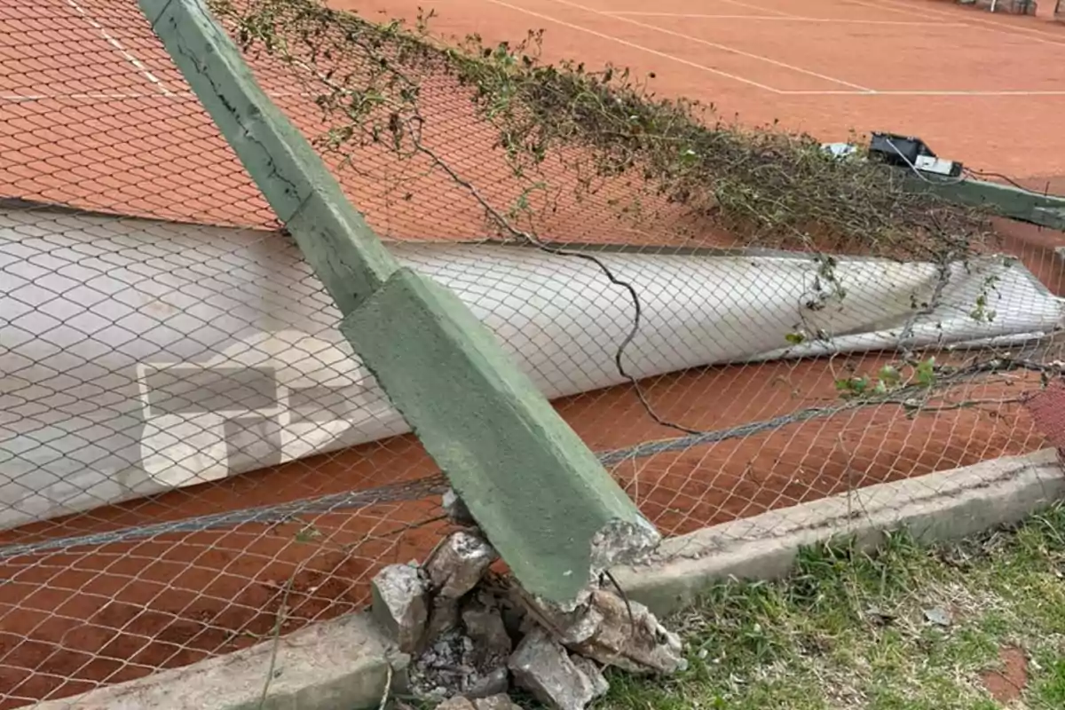 A fallen chain-link fence and a concrete post on a clay tennis court A fallen chain-link fence and a concrete post on a clay tennis court