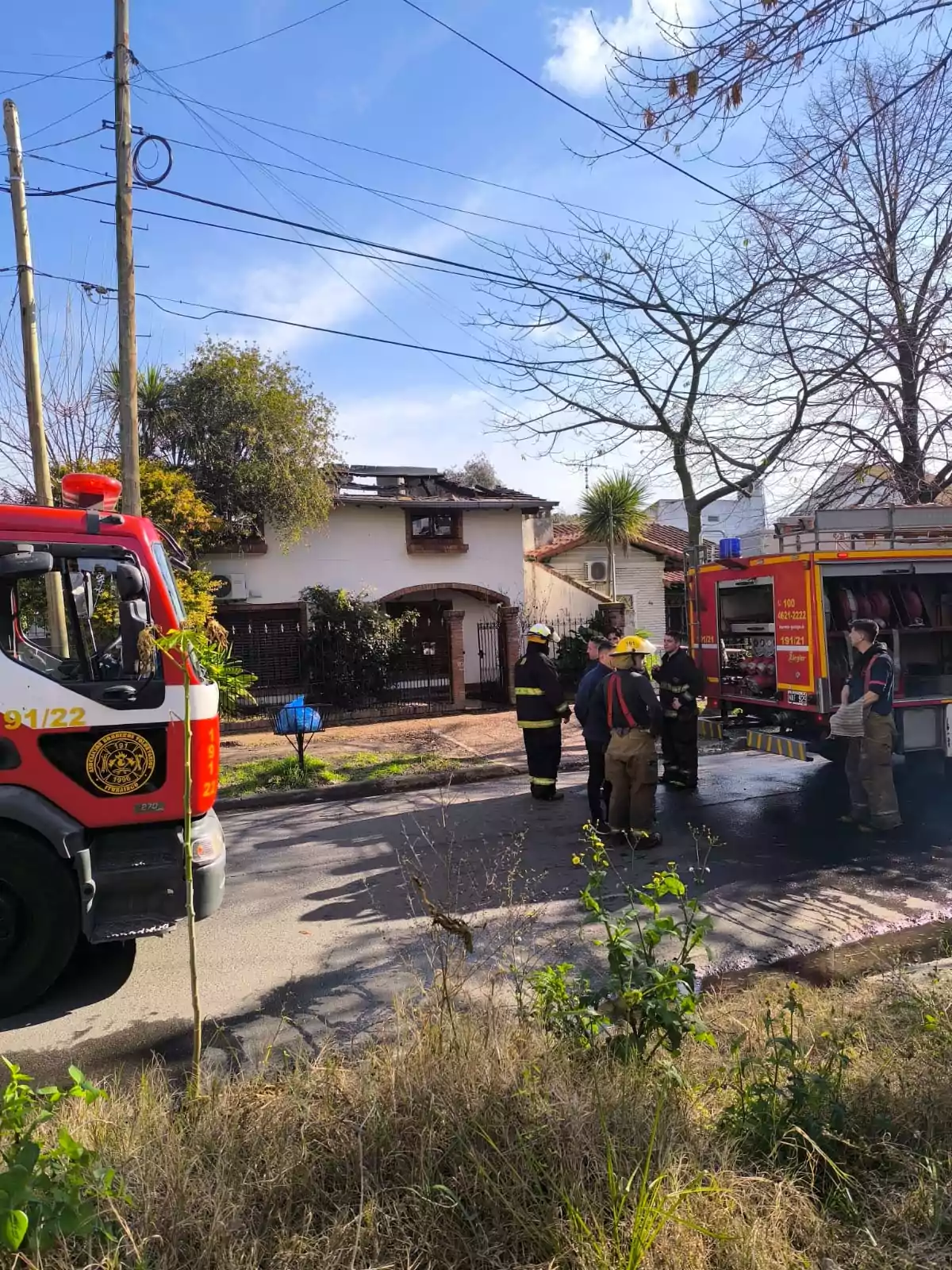 Firefighters and fire trucks in front of a house showing visible roof damage after a fire. Firefighters and fire trucks in front of a house showing visible roof damage after a fire.