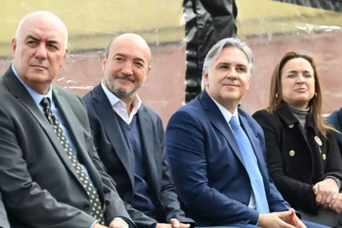 Cuatro personas sentadas usando ropa formal observan hacia el frente en un evento al aire libre