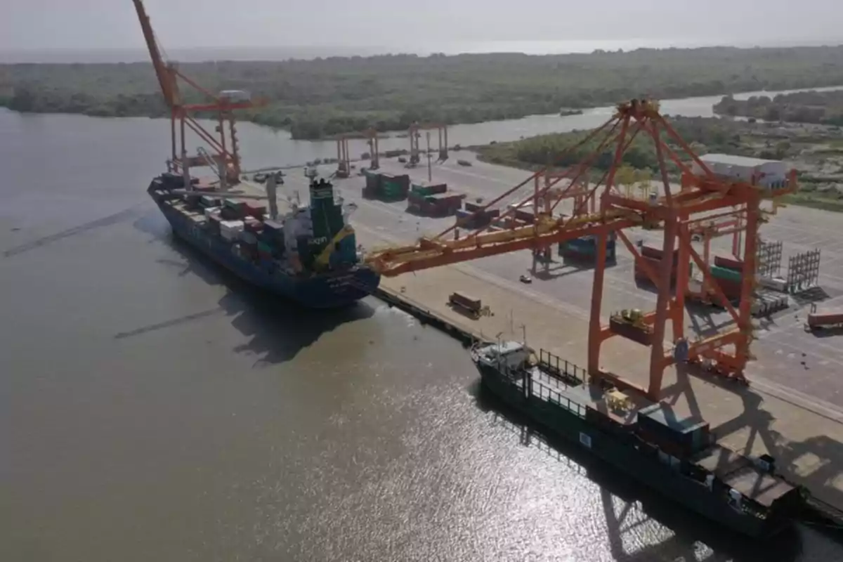Barco de carga atracado en un puerto con grúas naranjas y contenedores apilados en la terminal