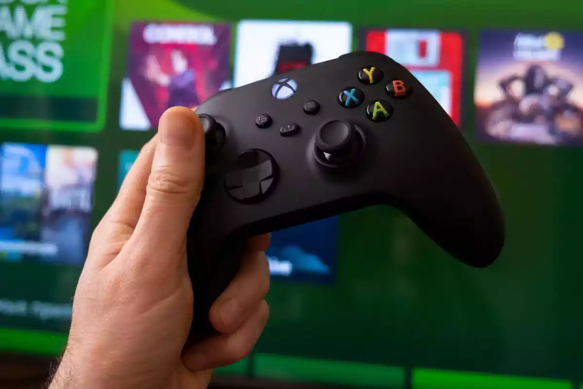 Persona sosteniendo un control de Xbox frente a una pantalla con videojuegos. Persona sosteniendo un control de Xbox frente a una pantalla con videojuegos.