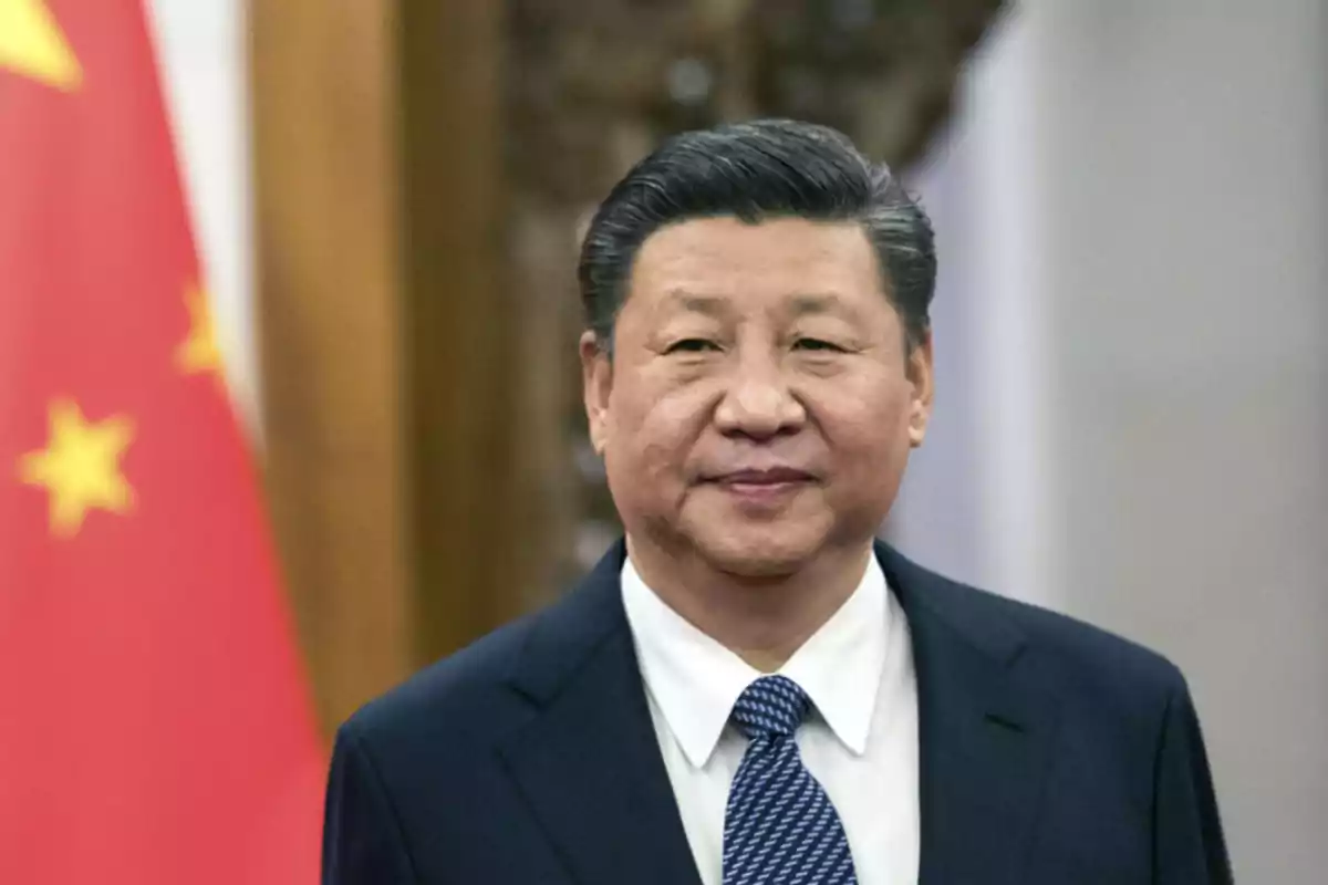 Hombre de traje oscuro y corbata azul posando frente a una bandera de China desenfocada al fondo Hombre de traje oscuro y corbata azul posando frente a una bandera de China desenfocada al fondo