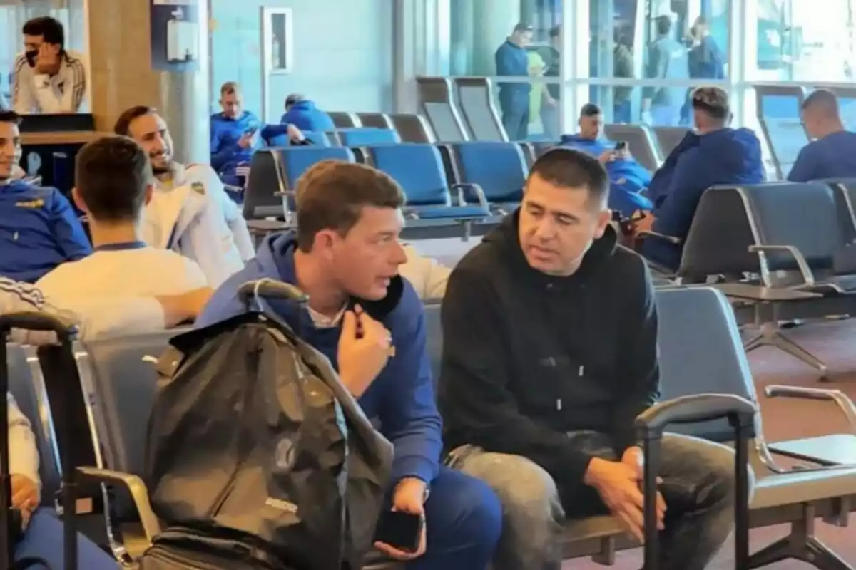 Varias personas con ropa deportiva conversan y esperan sentadas en una sala de aeropuerto, algunas con maletas y mochilas. Varias personas con ropa deportiva conversan y esperan sentadas en una sala de aeropuerto, algunas con maletas y mochilas.