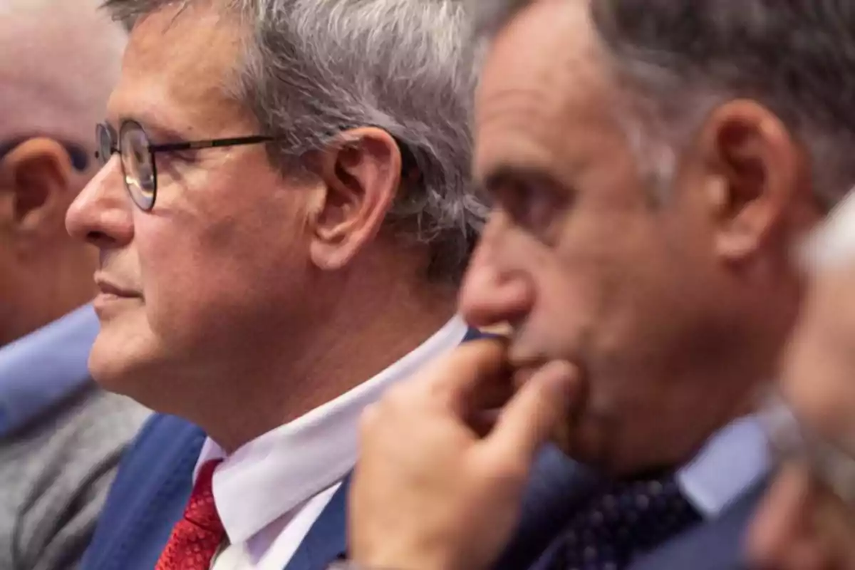 Middle-aged men in suits and ties sitting in a row, paying attention to an event Middle-aged men in suits and ties sitting in a row, paying attention to an event