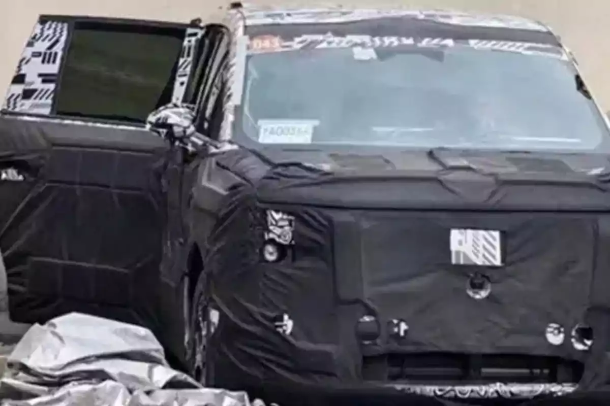 Vehicle covered with black camouflage during testing, with the driver’s door open and details concealed to prevent revealing its design. Vehicle covered with black camouflage during testing, with the driver’s door open and details concealed to prevent revealing its design.