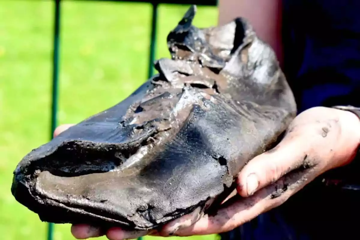 Persona sosteniendo un zapato antiguo y deteriorado cubierto de lodo Persona sosteniendo un zapato antiguo y deteriorado cubierto de lodo