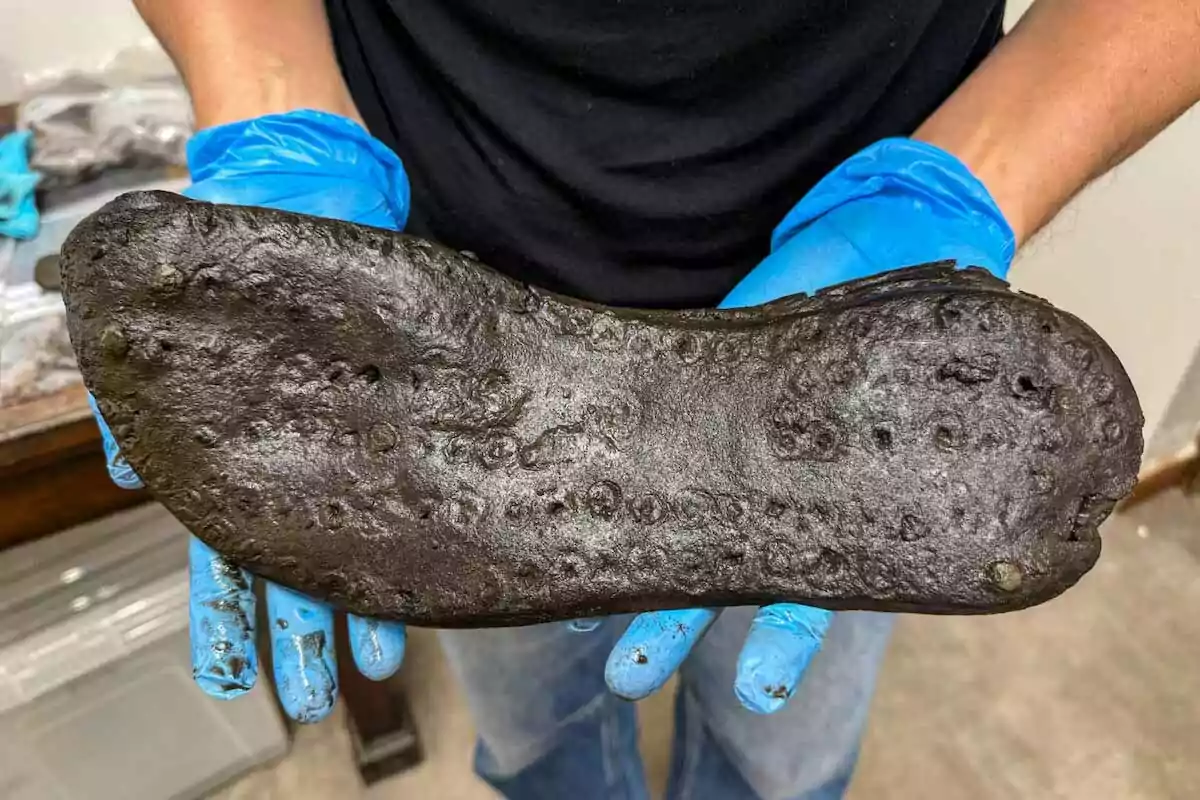 Persona con guantes azules sostiene una suela antigua de zapato de aspecto oscuro y desgastado Persona con guantes azules sostiene una suela antigua de zapato de aspecto oscuro y desgastado