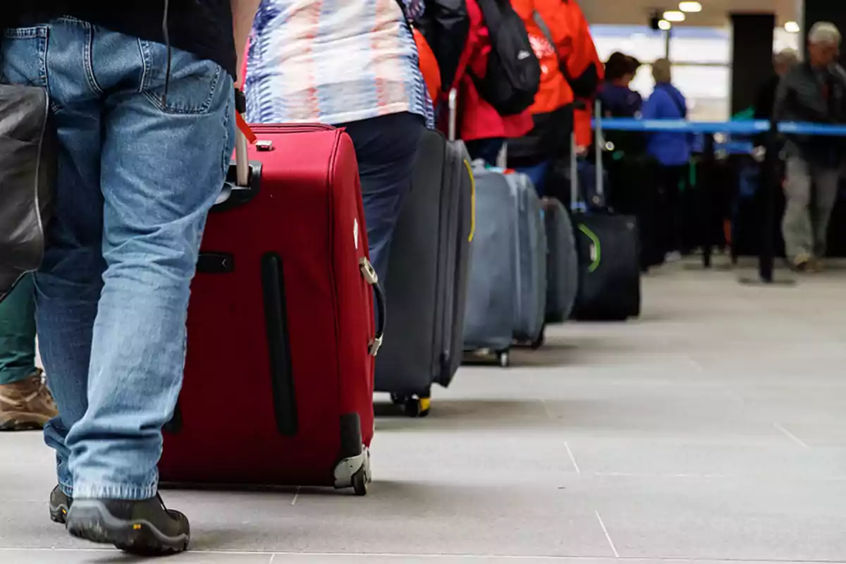 Personas haciendo fila con maletas en un aeropuerto