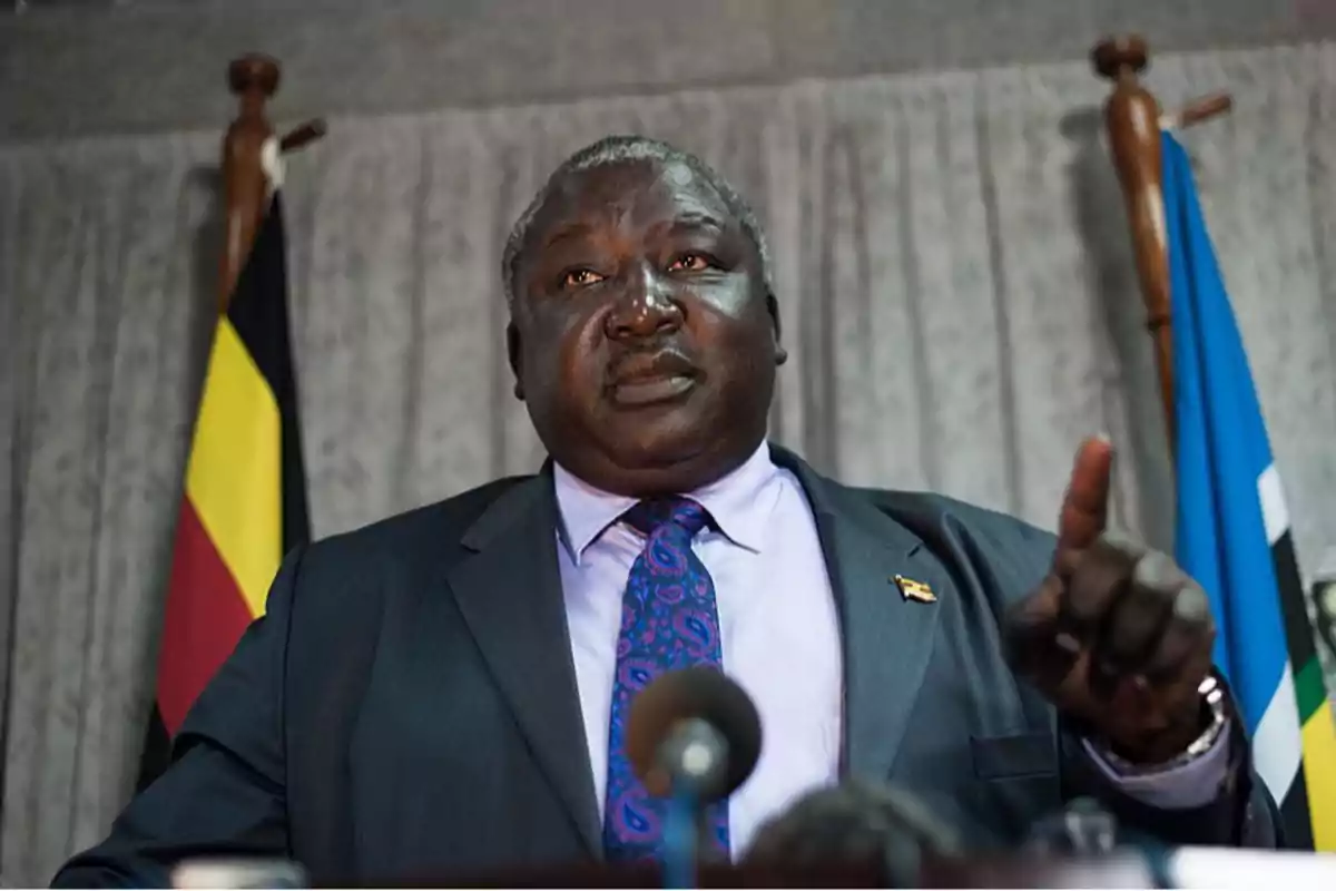 Man in a suit and tie speaking at a press conference with flags in the background Man in a suit and tie speaking at a press conference with flags in the background