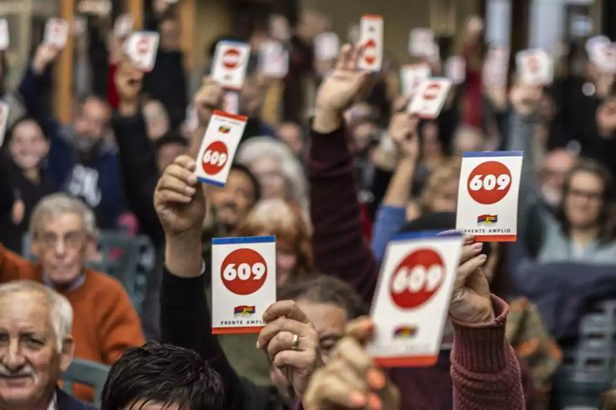 Personas en una asamblea levantan tarjetas con el número 609 y el logo del Frente Amplio Personas en una asamblea levantan tarjetas con el número 609 y el logo del Frente Amplio