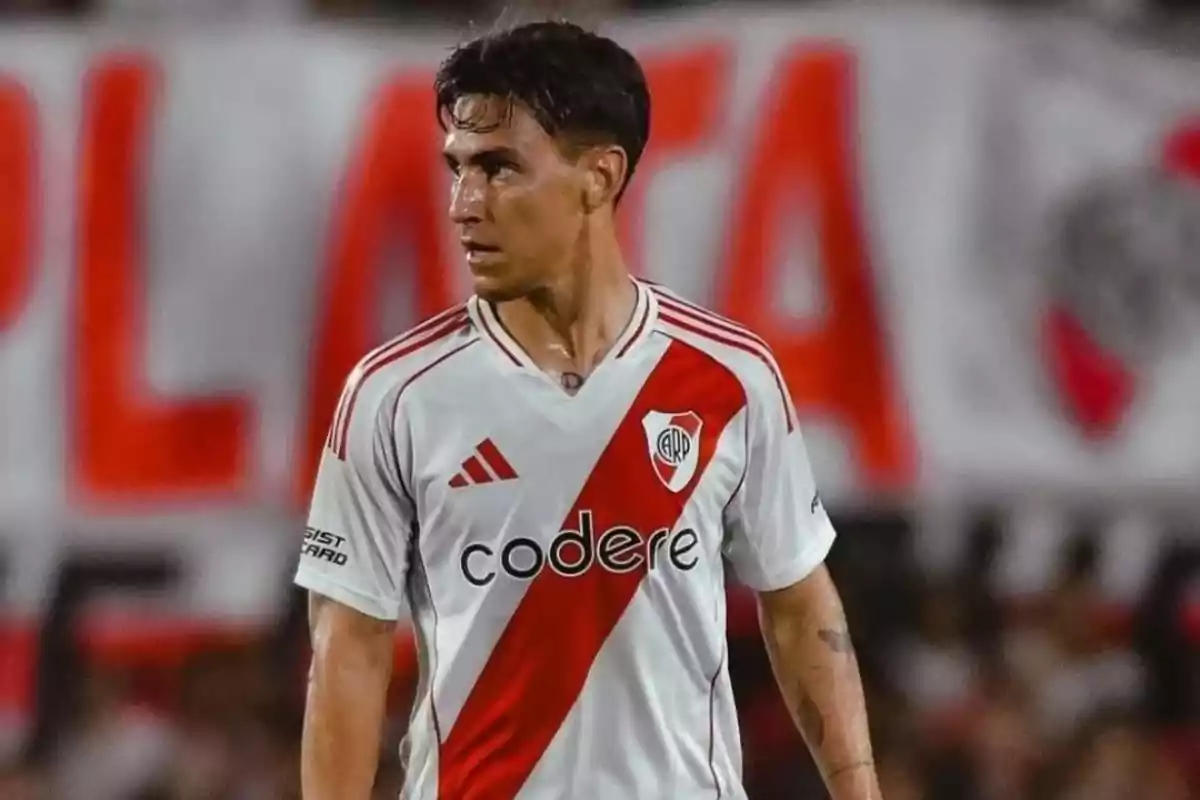Soccer player wearing a white River Plate jersey with a red stripe in a stadium