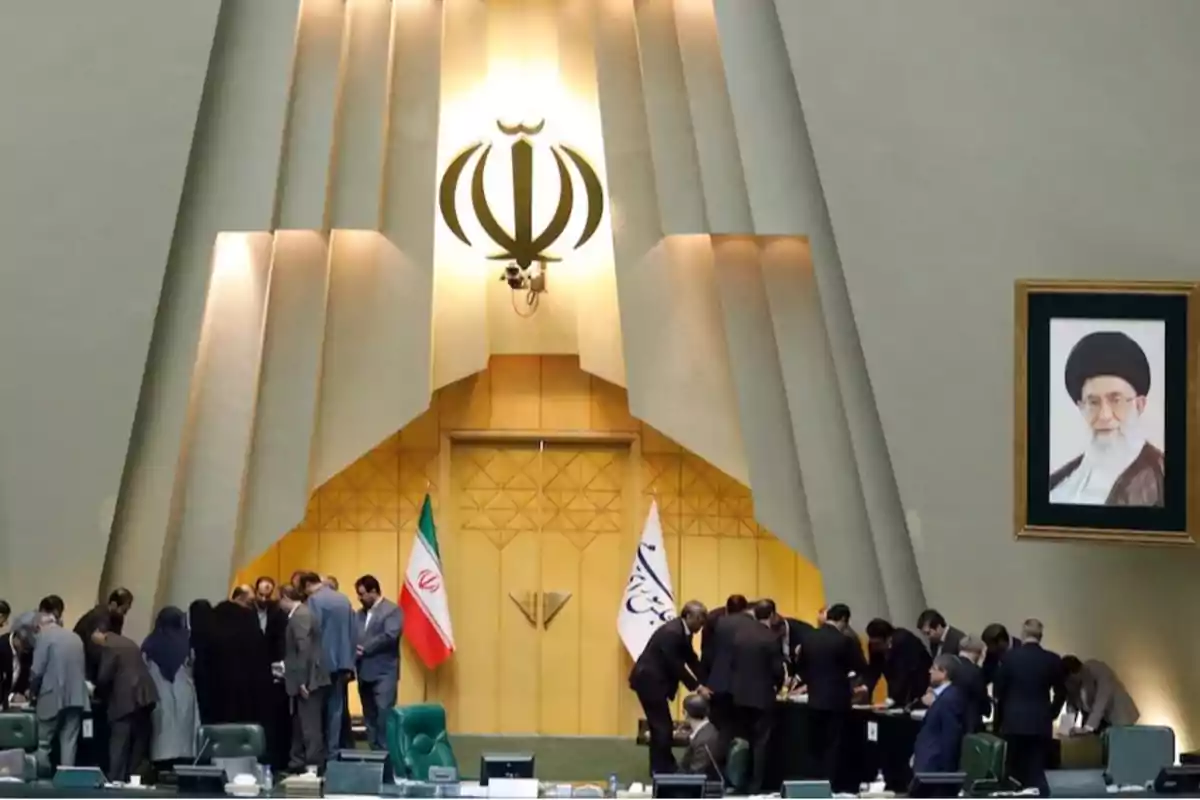 Personas reunidas en el interior de un parlamento con banderas de Irán y un retrato en la pared
