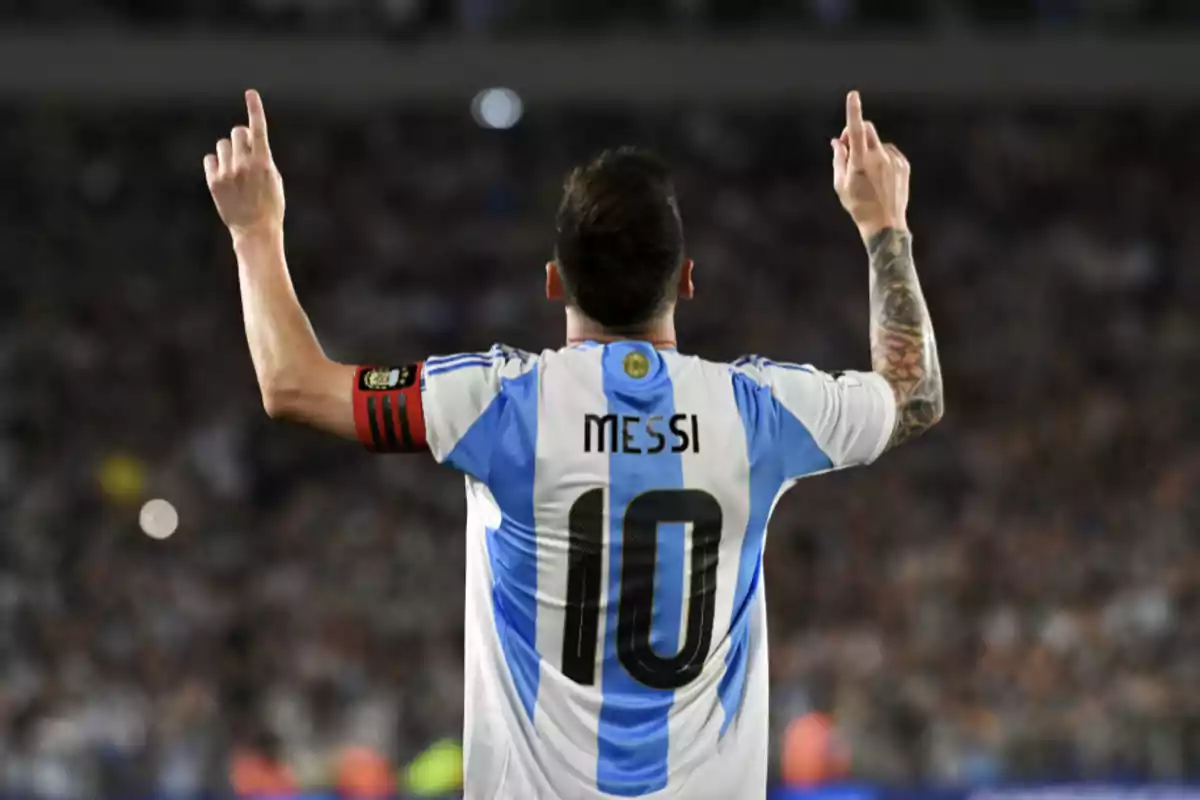 Futbolista argentino con la camiseta número 10 levantando ambos brazos y señalando hacia arriba en un estadio lleno de público