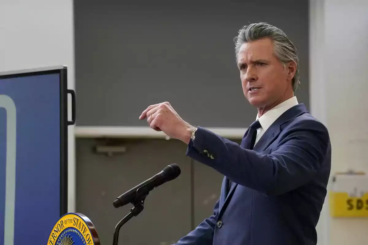 Hombre de traje azul hablando en un podio con micrófono y haciendo un gesto con la mano Hombre de traje azul hablando en un podio con micrófono y haciendo un gesto con la mano
