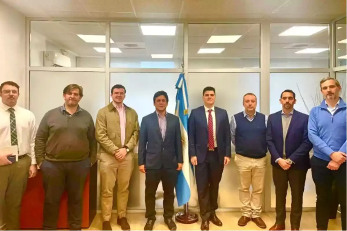 Ocho hombres posan de pie en una oficina junto a una bandera de Argentina