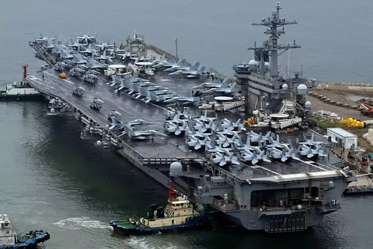Portaaviones militar en el mar con numerosos aviones de combate en la cubierta y varios remolcadores alrededor.