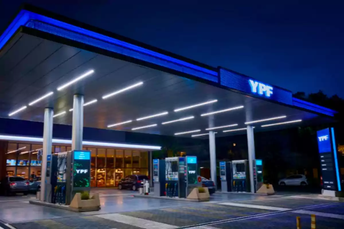 Estación de servicio YPF iluminada por la noche con varios surtidores y autos estacionados